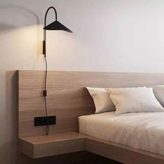 a bed with white sheets and pillows next to a wall mounted light on the side