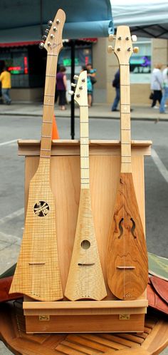 three wooden guitars sitting on top of a table next to each other and people walking in the background