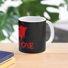 a black and red coffee mug sitting on top of a wooden table next to a book