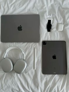 two apple laptops and headphones on a white sheet with earbuds next to each other