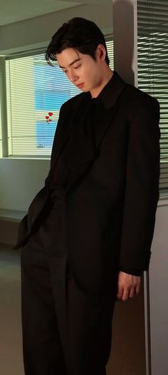 a man in a black suit leaning against a wall