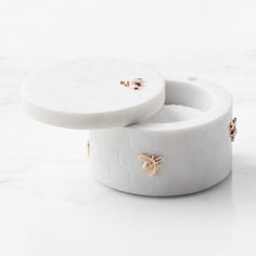 two white boxes with gold bee studs on them sitting on a marble countertop