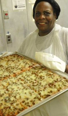 a woman holding up a large pan of pizza