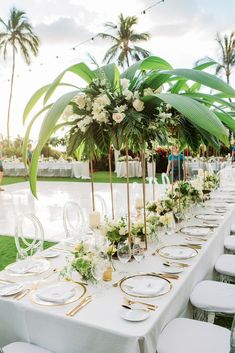 a long table is set up with white and gold place settings for an outdoor wedding