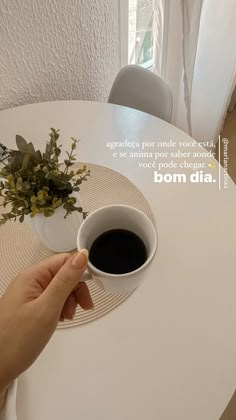 a person holding a cup of coffee on top of a white table next to a potted plant