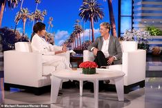 two people sitting on white couches in front of a tv screen with palm trees