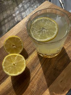 two lemons are sitting on a cutting board next to a glass with water and ice