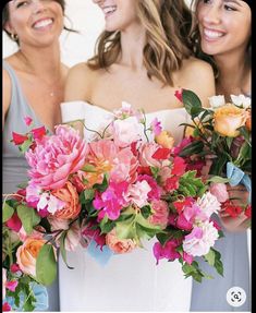 three beautiful women standing next to each other holding flowers