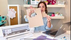 a woman sitting at a desk with a laptop and paper in front of her face