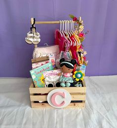 a wooden crate filled with baby items on top of a white sheet covered bed next to a purple wall