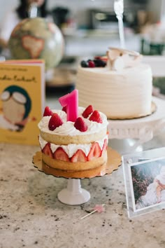 two cakes with strawberries and cream frosting sitting on a counter next to photos