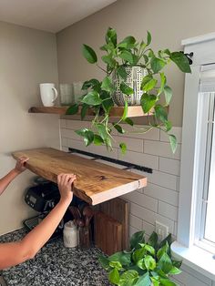 a woman is working on a wooden shelf with plants hanging from the top and below