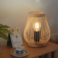 a wooden table with a lamp on it and a plate next to it, near a plant