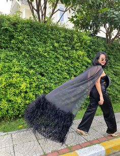 a woman is walking down the sidewalk with a black cape on her head and an ostrich tail