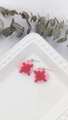 pink and red heart shaped earrings sitting on top of a white tray next to green leaves