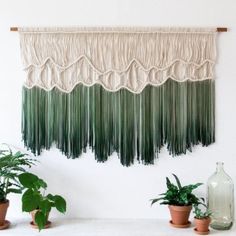 three potted plants are sitting in front of a wall hanging with fringes on it