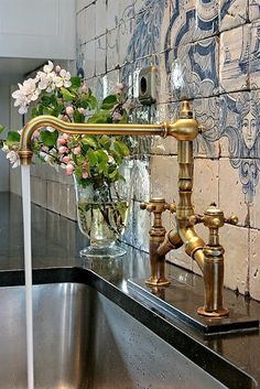 a gold faucet with flowers in a glass vase on a counter top next to a sink