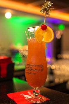 an orange drink with a garnish on top sits on a table in a bar