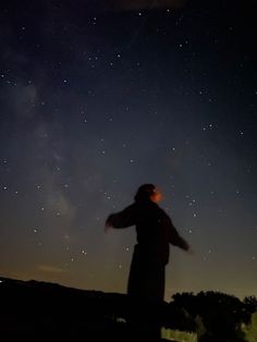 a person standing in the dark with their arms spread out looking up at the stars