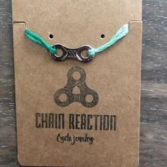 the chain reaction bracelet is attached to a brown card with green string and silver clasps