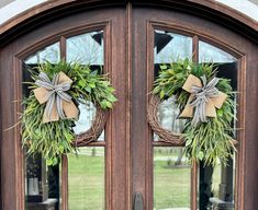 two wreaths on the front door of a house decorated with greenery and bows