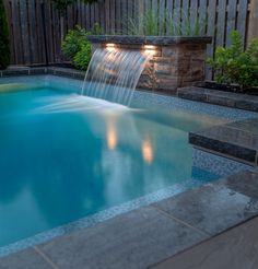 a small pool with a waterfall in the middle and lights on it's sides