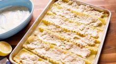 a pan filled with pasta and sauce next to a bowl of lemons on a wooden table