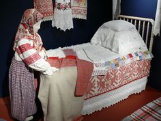 a doll is standing next to a crib with clothes hanging on the wall and two bedspreads