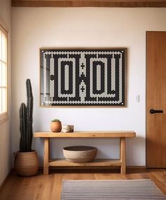 a wooden table sitting in front of a painting on the wall next to a cactus