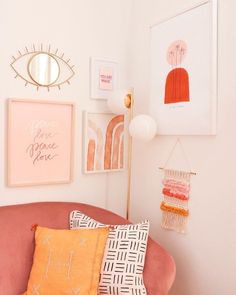 a pink couch with pillows and pictures hanging on the wall above it, along with other decorative items