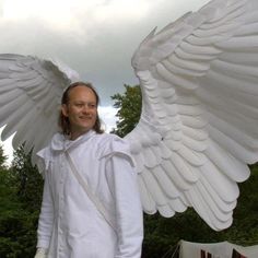 a man dressed as an angel stands in front of some tents with large white wings