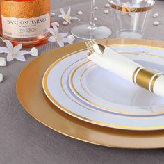 there is a bottle of booze on the table next to two plates with gold rims