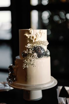 a three tiered cake with white flowers and disco ball decorations on the top layer