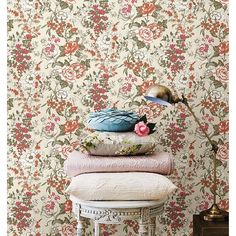 a stack of pillows sitting on top of a table next to a lamp and flower wallpaper