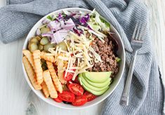 a white bowl filled with meat, cheese and veggies next to a fork