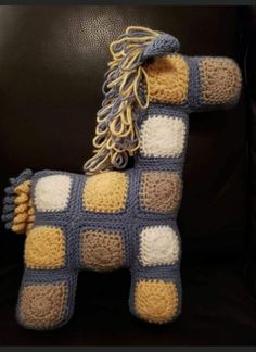 a crocheted toy horse is sitting on a black leather chair with yellow and white squares