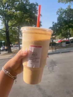 a person holding up a drink with a straw in it's hand on the street