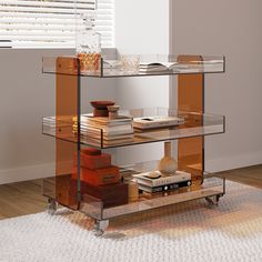 a glass shelf with books and other items on it next to a rug in front of a window