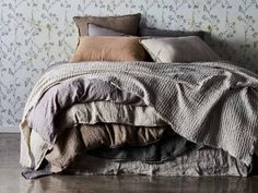 an unmade bed with several pillows and blankets on it, in front of a floral wallpaper