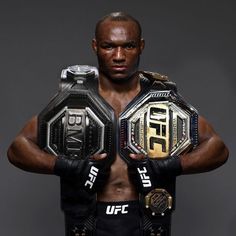 a man with his hands on his hips holding up two different wrestling belts in front of him