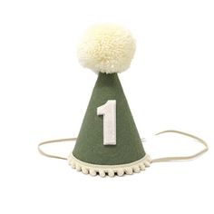 "Small 3\" or Large 5\" Olive Green Wool Felt hat, Cream yarn pom, Cream pom trim, with or without Linen Felt number backed in Linen. Our party hats and crowns are attached to a comfortable elastic and meant to be worn around the back of the head, behind the ears. Tilt to the side for a fun, whimsical look! LITTLE BLUE OLIVE SHOP CROWNS and HATS are the perfect accessory for birthday celebrations, memorable photo shoots and every day fun for dress up. Hats are hand crafted of a high quality, non First Birthday Party Hat, First Birthday Neutral, Green First Birthday, Felt Party Hat, Green Birthday Party, First Birthday Hat, Neutral Party, Boys First Birthday, Hat Cream