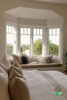 a bed sitting under two windows next to a window sill with pillows on it