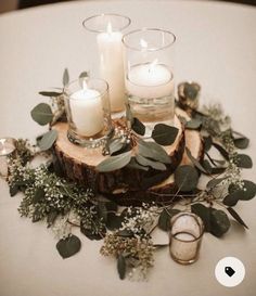 candles and greenery are arranged on top of a wood slice for a centerpiece