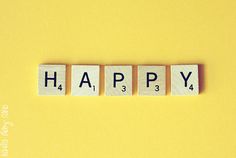 the word happy spelled with scrabble blocks on a yellow background, top view