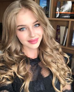 a woman with long blonde hair and blue eyes posing for a photo in front of bookshelves