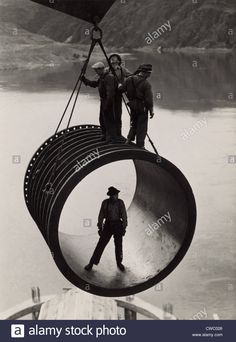 two men standing on top of a large metal object in the air near water and mountains