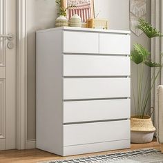 a white chest of drawers sitting in a room next to a potted plant and door