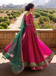 a woman in a pink and green lehenga stands on a balcony overlooking the city