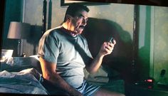 a man sitting on a bed holding a cell phone in his hand and looking at the screen