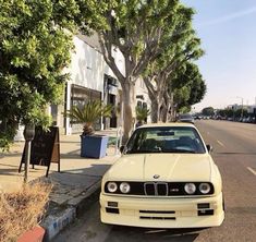 a white car parked on the side of a street next to a tree lined sidewalk